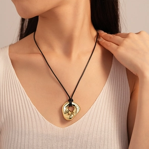 Close-up of golden irregular fluid heart pendant with black cord on model neck