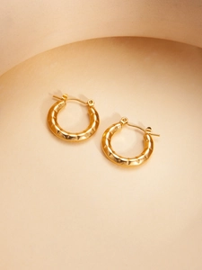 Macro detail of golden hoop earrings featuring unique irregular hammered metal textures