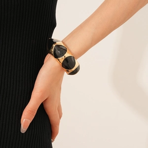 Close-up of wide gold-plated cuff bracelet featuring black enamel geometric patterns