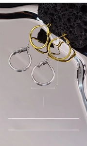 Detail of 30x25mm large hoop earrings in gold and silver finish on a textured surface