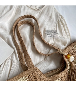 Close-up of woven straw tote bag featuring wide strap and tassel with amber bead detail