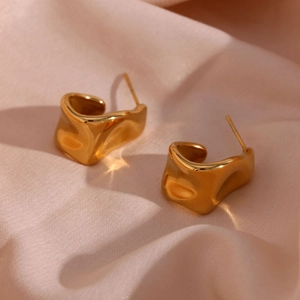 Macro shot of gold irregular wrinkled earrings on soft pink satin fabric background