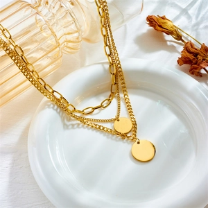 Layered gold titanium steel necklace with multiple chains and coin pendants on a white plate