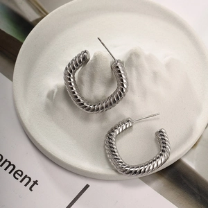 Detailed view of silver C-shaped twist hoop earrings on a minimalist display stand