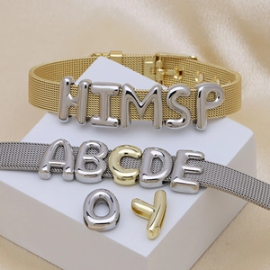 Dettaglio di bracciali a maglia regolabili in oro e argento con ciondoli a lettere