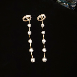 Detail view of golden CD letter earrings with long white dangling pearl chains