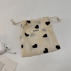 Close-up of a beige drawstring pouch with black heart patterns and brand label