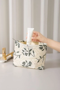 Detail of floral embroidery on a linen makeup bag with hand putting in cream