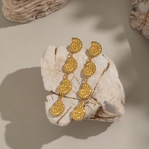 Gold plated stainless steel drop earrings with four linked shell pendants on a rock