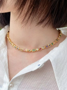 Detail of a gold necklace with colorful round and oval gemstones worn by a model