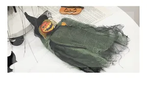 Detail of Halloween witch doll with pumpkin head, green mesh robe and wooden broom prop