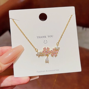 Detail of gold necklace featuring pink flower pendant and teardrop crystal on a card