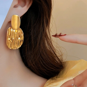 Détail de boucles d'oreilles dorées texturées au fini métallique plissé sur un mannequin