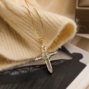 Detail of 18K gold-plated cross pendant necklace with zircon stones on knit fabric