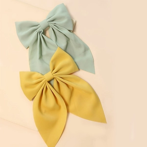 Detail of solid color bow hairpins in light green and yellow fabric on beige background