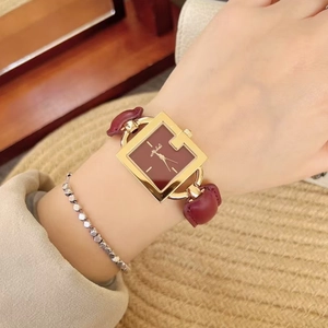 Close-up of elegant square gold watch with deep red leather strap and matching dial