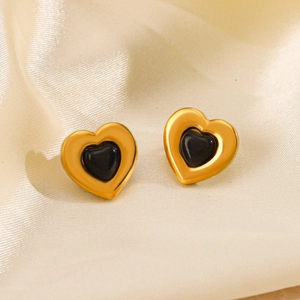 Golden heart-shaped stud earrings with inlaid black gemstone on elegant silk background