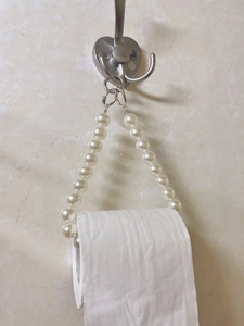 Detail of white beaded toilet paper holder with pearls and metal rings on marble wall