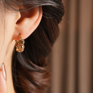 Nahaufnahme eleganter goldener Creolen mit bernsteinfarbenen Kristallen an einem Model