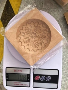 Square beechwood cookie mold with carved floral patterns shown on an electronic scale