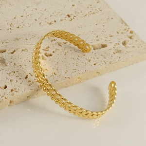 Bracelet jonc ouvert en acier inoxydable tressé plaqué or 18K sur une surface en travertin