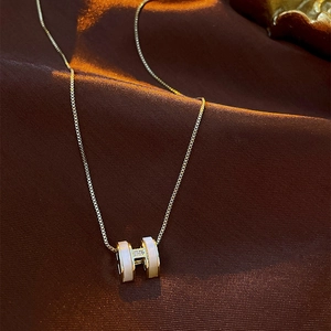 Macro shot of gold H-shaped pendant necklace with white enamel and sparkling zircons