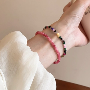 Detail von rosa Erdbeerkristall und bunten Perlenarmbändern am Handgelenk einer Frau