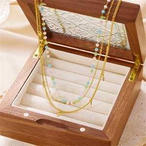 Close-up of triple-layer gold necklace with colorful beads and small cross charms