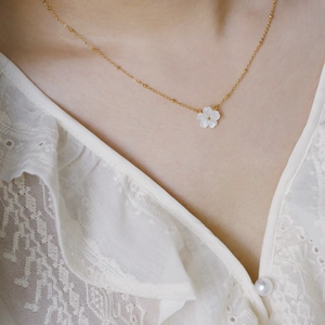 Detail of Saturn chain gold necklace with white shell flower pendant on a model
