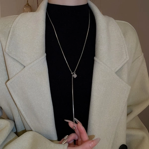 Close-up of a silver Y-shaped long necklace with flower pendant on a black sweater