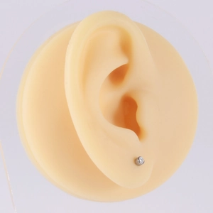 Titanium silver round ear stud with a tiny clear gemstone shown on a model ear