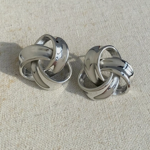 Detail view of silver twisted geometric knot earrings on textured fabric background