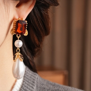 Detail of vintage gold earrings with red stones and baroque pearls worn by a model