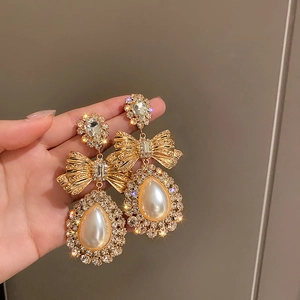 Détail de boucles d'oreilles nœud avec perles et cristaux tenues à la main