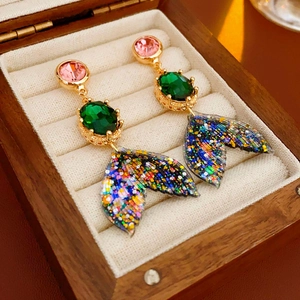 Détail de boucles d'oreilles queue de poisson colorées avec pierres roses et vertes