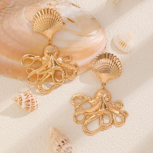 Detailed close-up of golden octopus seashell earrings on white beach sand and shells