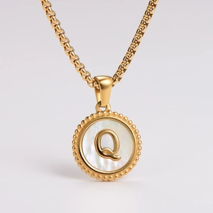 Detail of gold necklace featuring a round white shell pendant with letter Q engraving