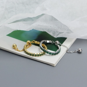 Close-up of gold and silver adjustable rings with green stones and sliding chain