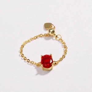 Adjustable gold plated link ring featuring an oval red zircon and heart charm pendant