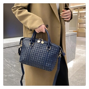 Détail macro du sac à main en cuir tressé bleu marine avec ferrures dorées et sangle
