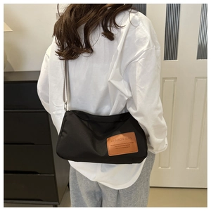 Detail of black nylon crossbody bag with adjustable gray strap and fashion patch