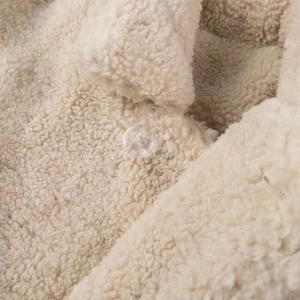 Detail shot of soft beige faux lamb wool fabric texture with a clear transparent button