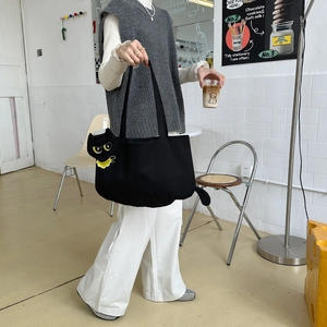 Detailed view of model wearing a black canvas tote with yellow cat embroidery