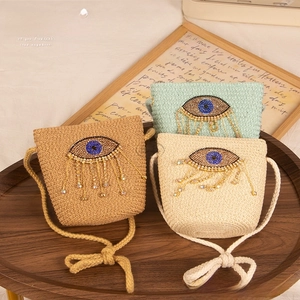 Detail of three woven evil eye crossbody straw bags with crystal tassels in warm setting