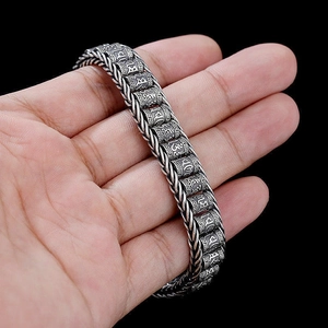 Gros plan d'un bracelet vintage en argent gravé des symboles du mantra à six syllabes.