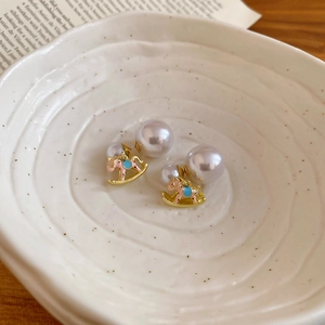 Detail shot of pearl rocking horse earrings with pink and blue enamel in a ceramic bowl