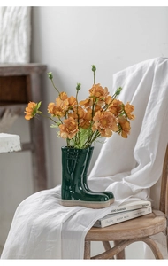 Creative green ceramic boot vase with orange flowers on a white vintage chair
