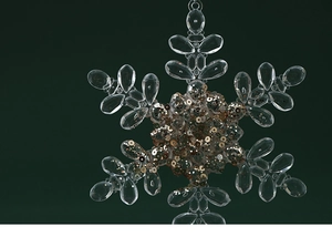 Close-up of acrylic snowflake ornament with gold sequins on dark green background