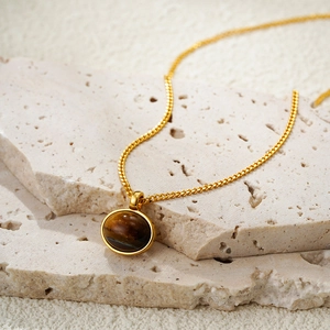 Elegant 18K gold plated necklace with oval tiger eye stone pendant on a textured stone base