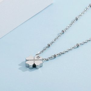 Macro shot of silver four-leaf clover pendant with small diamond and beaded chain